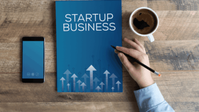 Caderno escrito Startup Business. Caneca de um lado e celular do outro.